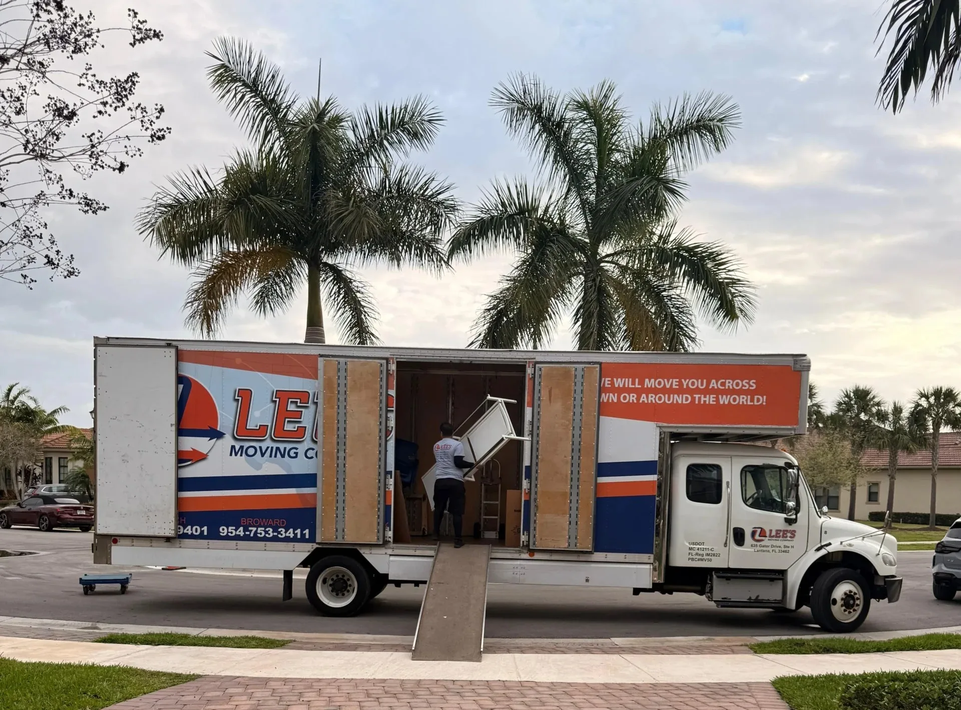 Lee's Moving Company crew actively unloading furniture from two trucks at a Boca Raton residential move
