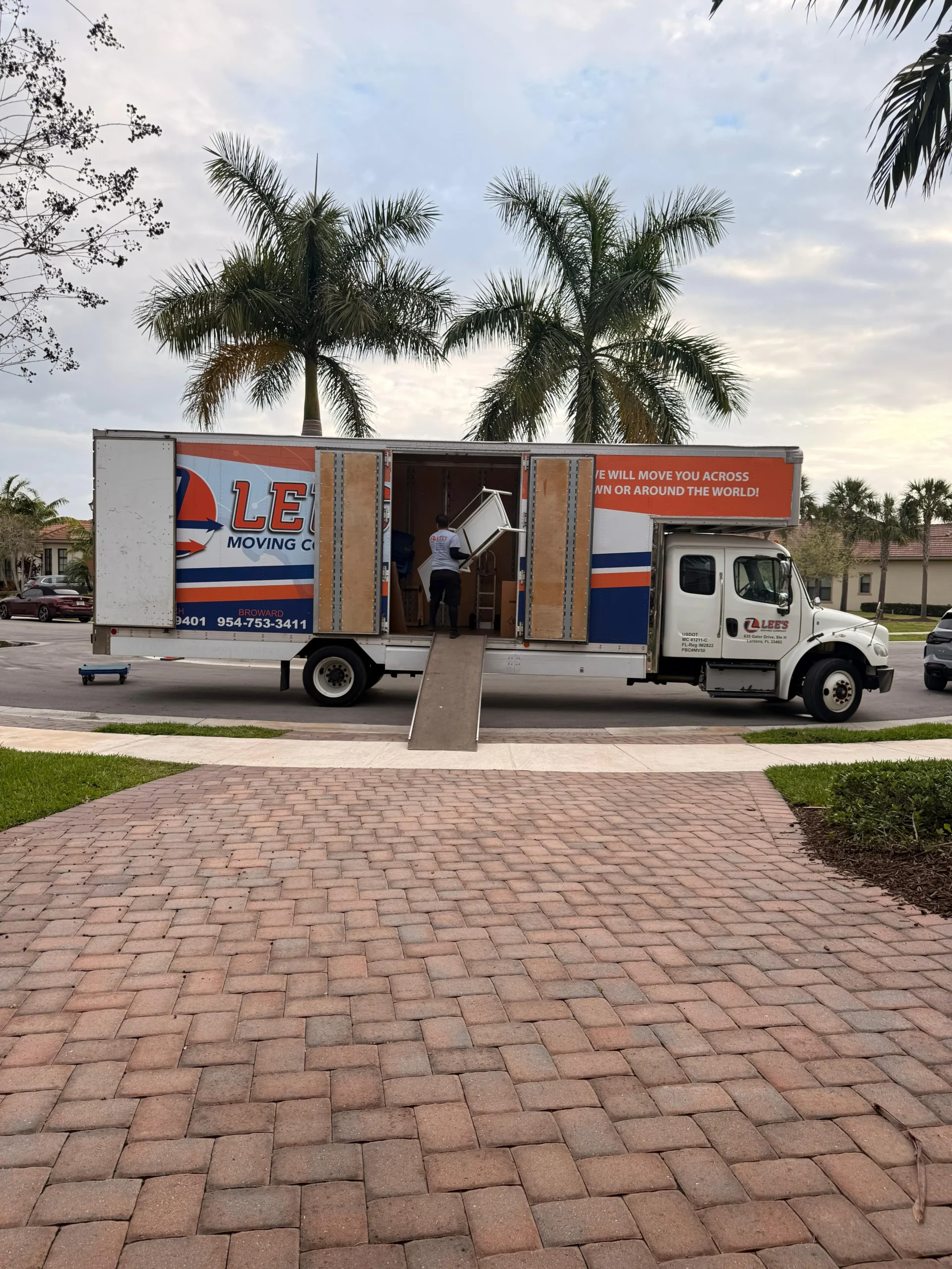 Lee's Moving Company crew actively unloading furniture from two trucks at a Davie residential move